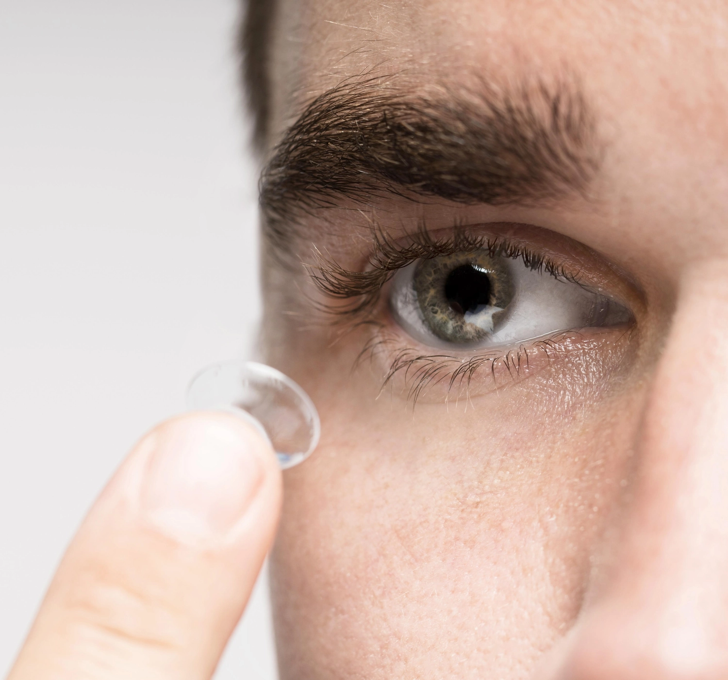 Kontaktlinsen Schmid - Kontaktlinsenspezialist und Sehtherapie - Eine Nahaufnahme zeigt das Auge einer Person und ihre Fingerspitze, die eine durchsichtige Kontaktlinse hält, die gleich eingesetzt wird.